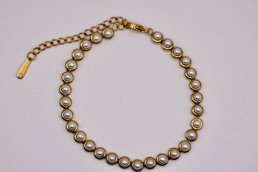 A gold-tone chain necklace featuring a series of small white faux pearls set in circular gold bezels, with a lobster clasp and extender chain on a plain light background.