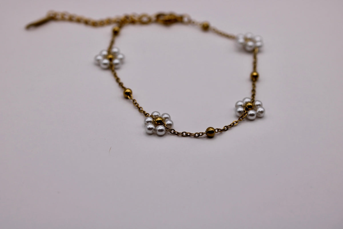 A delicate gold chain bracelet featuring small white pearl flower clusters and tiny gold beads, displayed on a plain light background.
