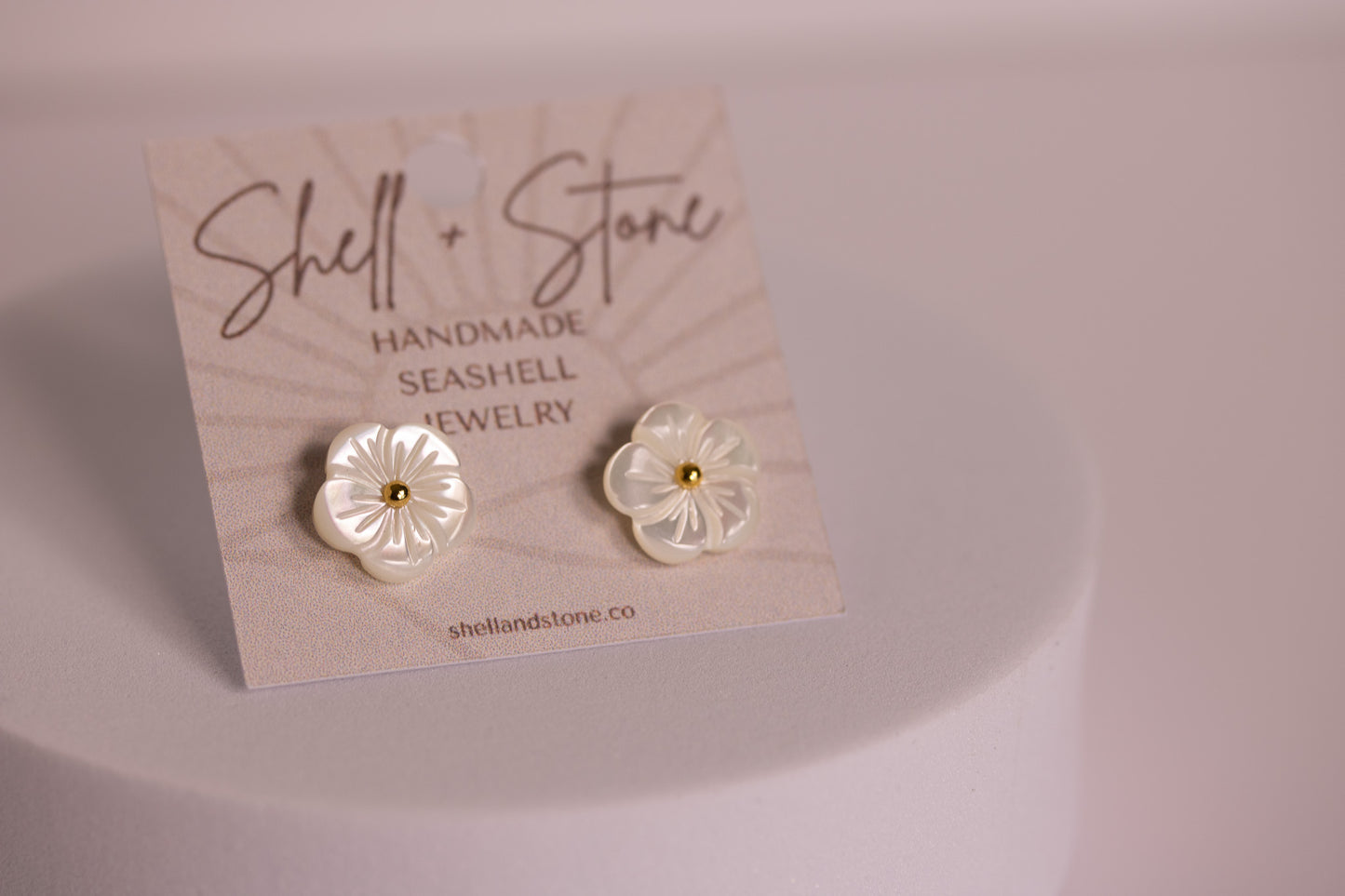Pair of flower-shaped earrings on a 'Shell + Stone' branded card.
