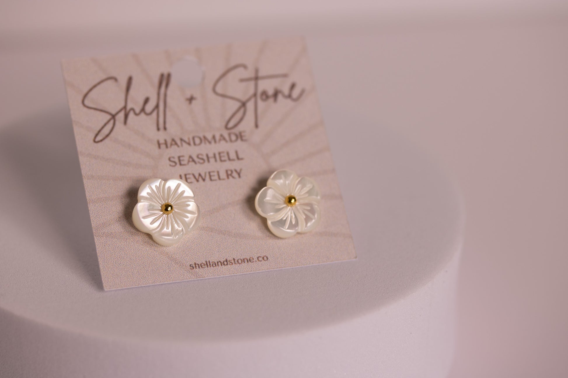 Pair of flower-shaped earrings on a 'Shell + Stone' branded card.