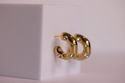 Gold hoop earrings with embedded stones on a light gray background