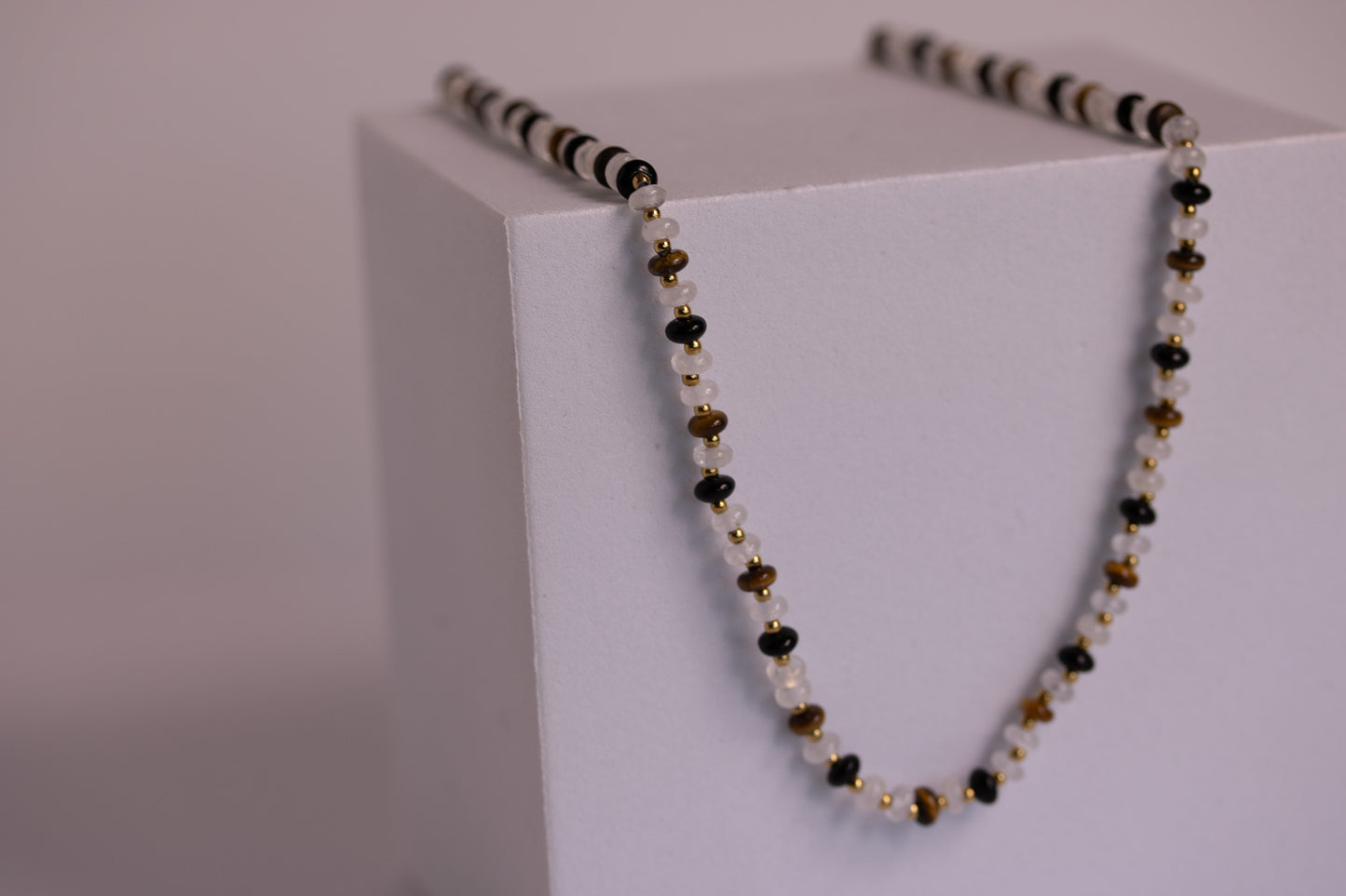 Necklace with black, gold, and white beads on a white block