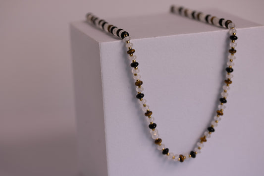 Necklace with black, gold, and white beads on a white block