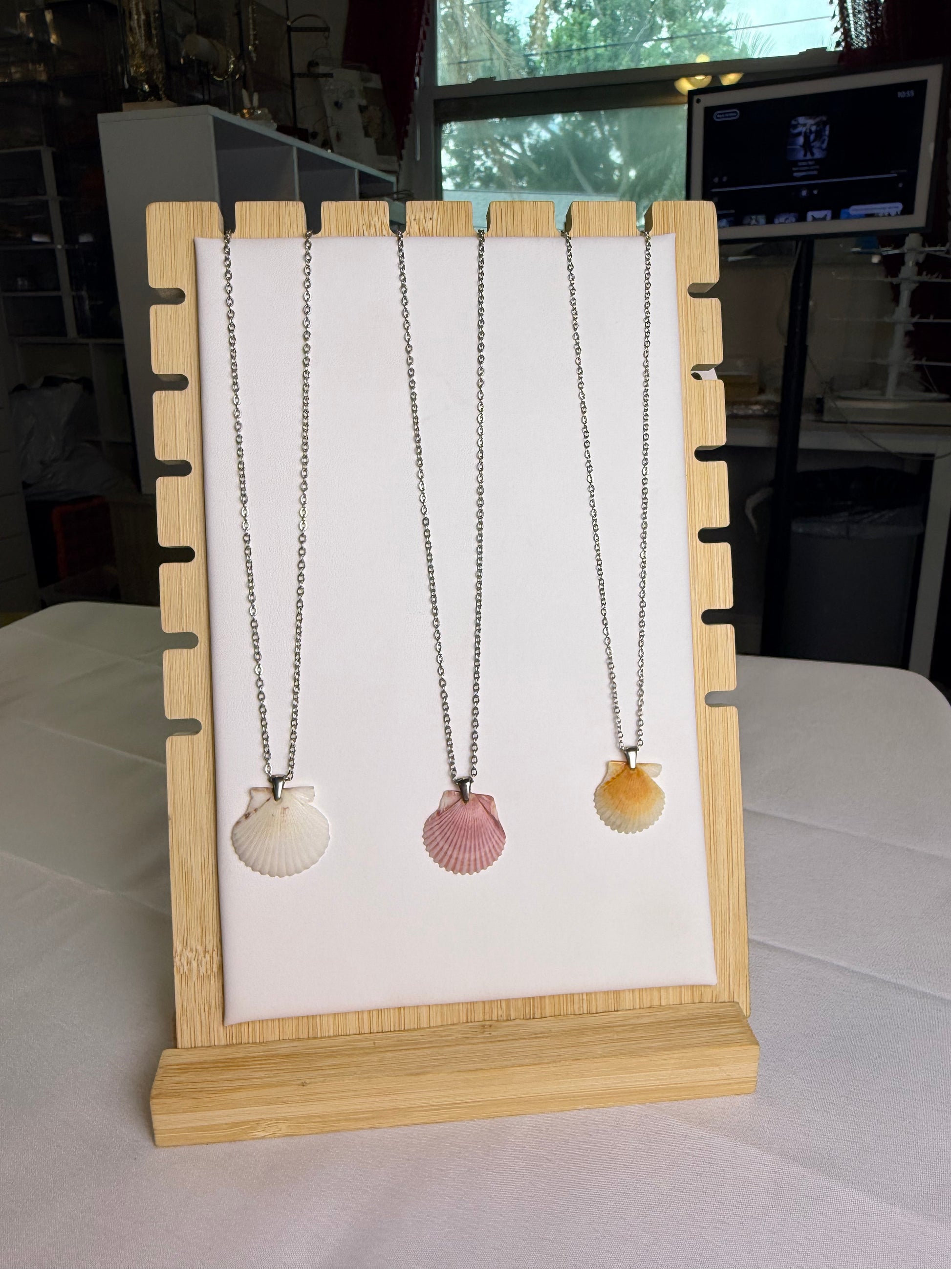 Three shell-shaped necklaces on a wooden stand with a white background