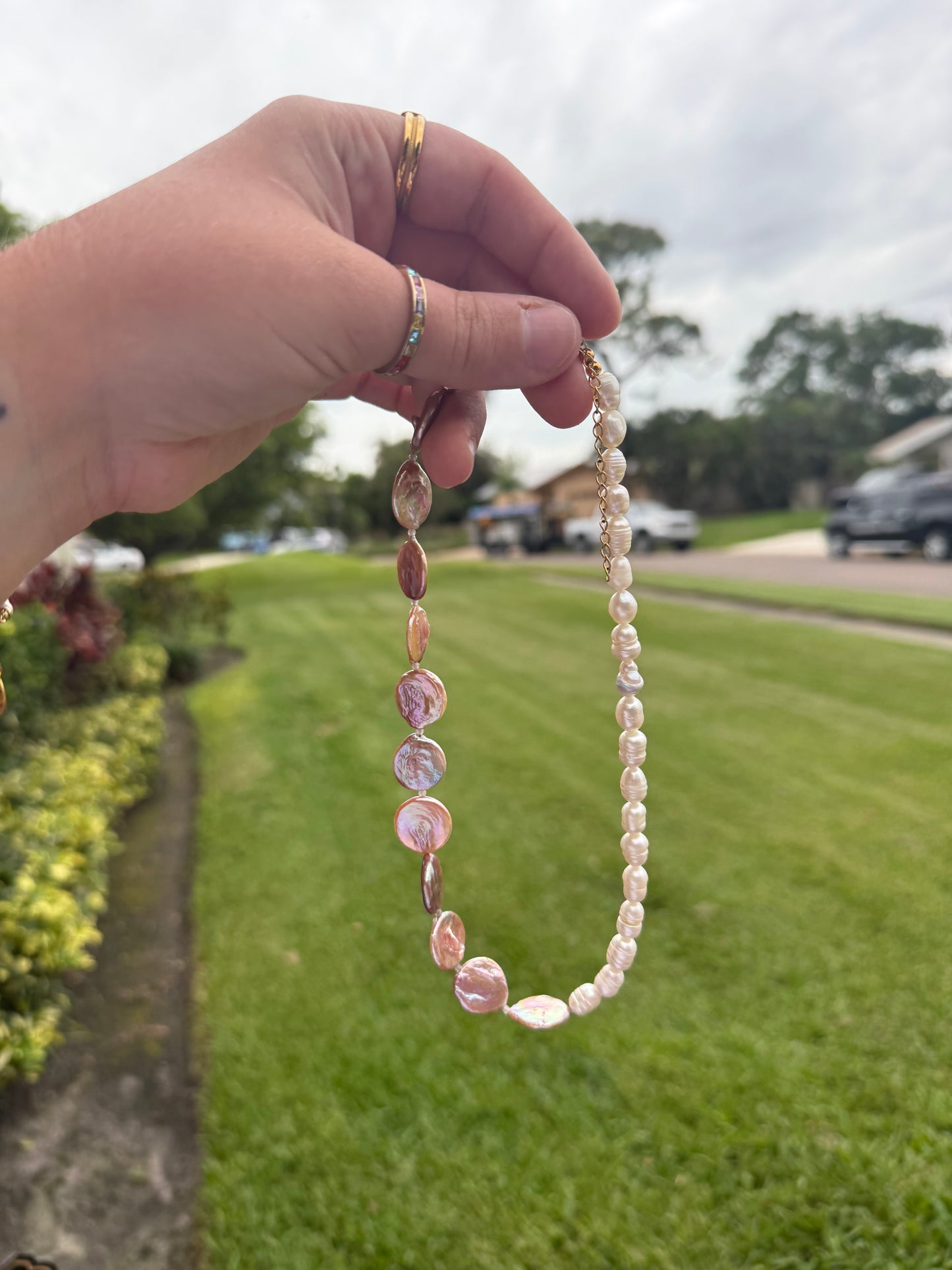 Hand holding a pearl necklace with a blurred outdoor background