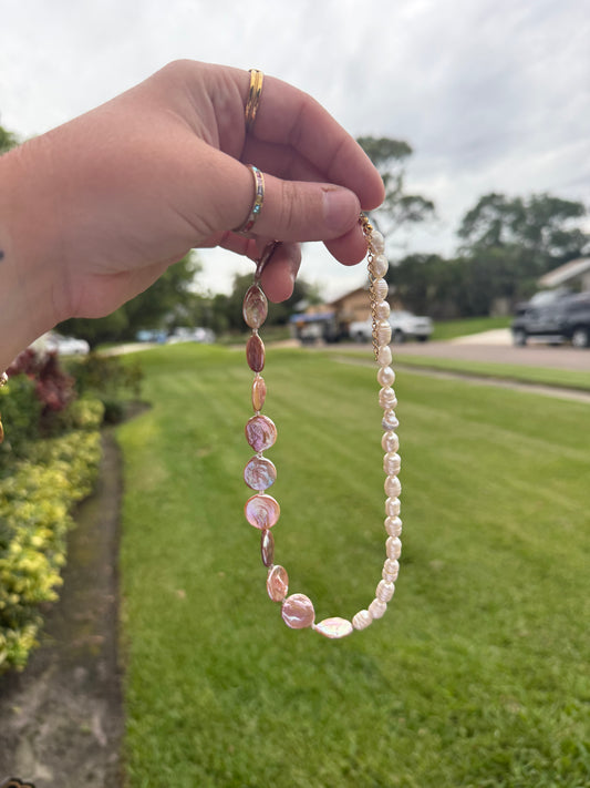 Hand holding a pearl necklace with a blurred outdoor background